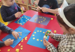 Dzieci układają 12 gwiazdek na wcześniej pomalowanym na niebiesko kartonie.